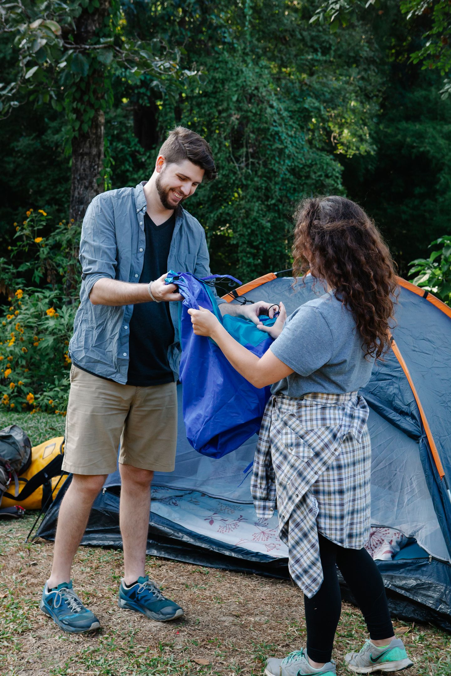 Two campers preparing their gear beside a tent in a wooded campsite