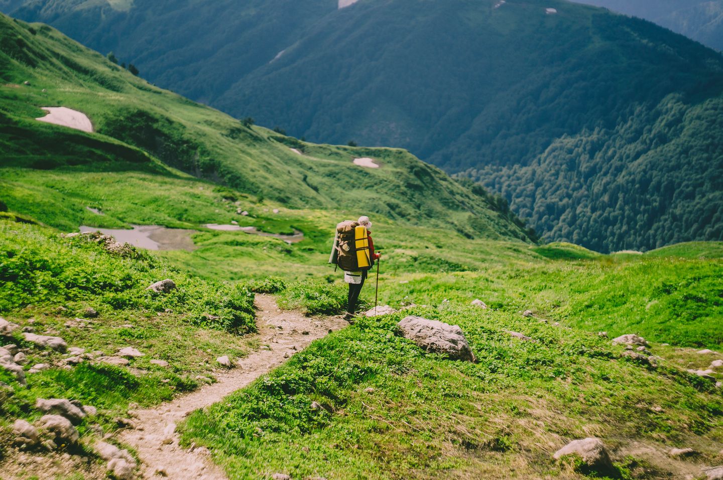 A hiker carrying a backpack along a green mountain trail