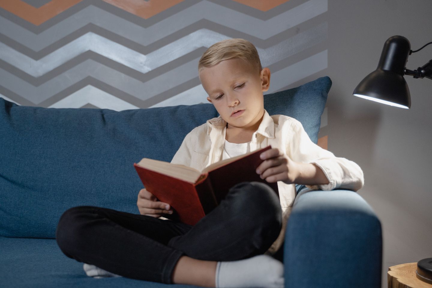A child reading on a sofa beneath a warm living-room lamp